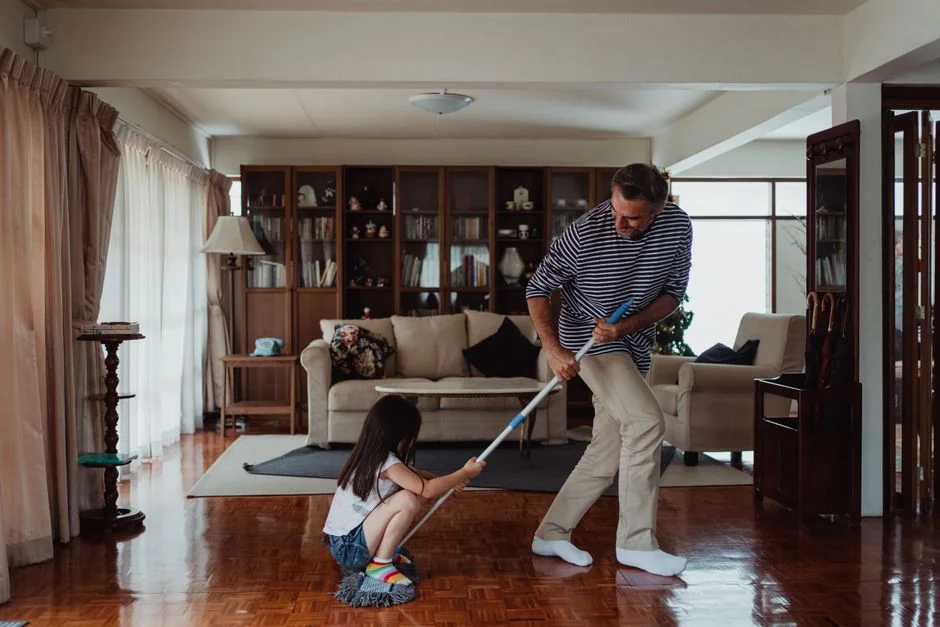 Two women in red overalls vacuuming and sweeping a modern living room.
